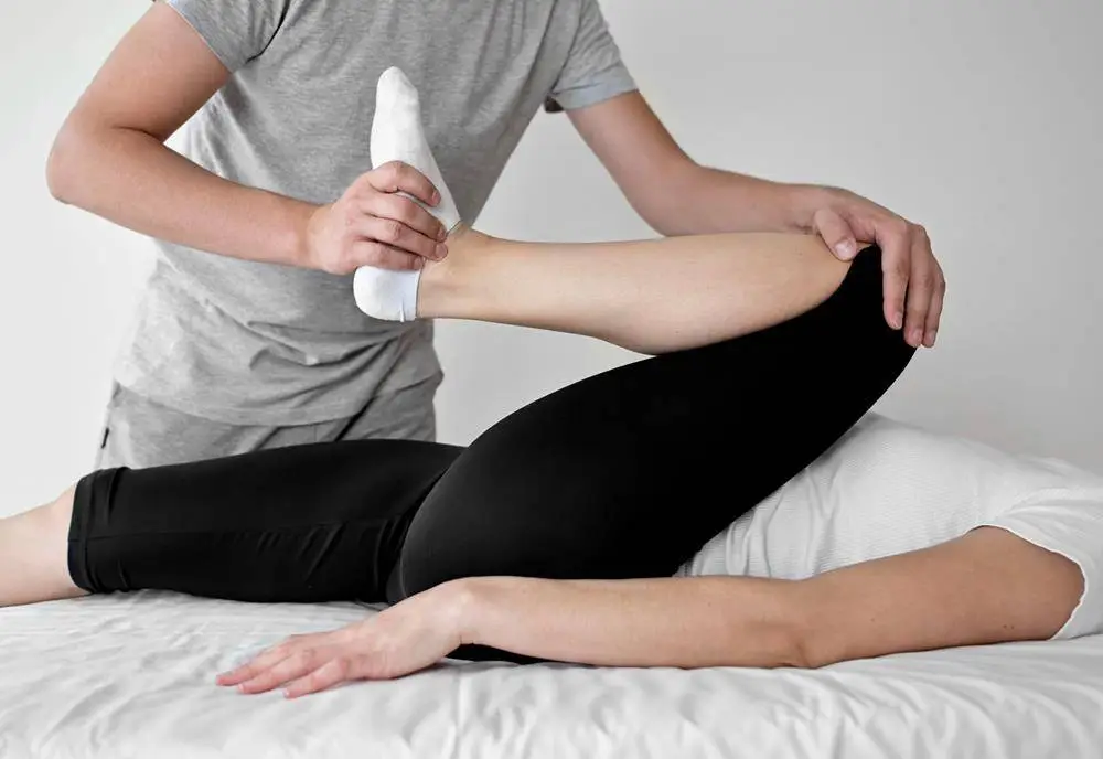 Physical therapist applying white ice pack to patient's leg during treatment session