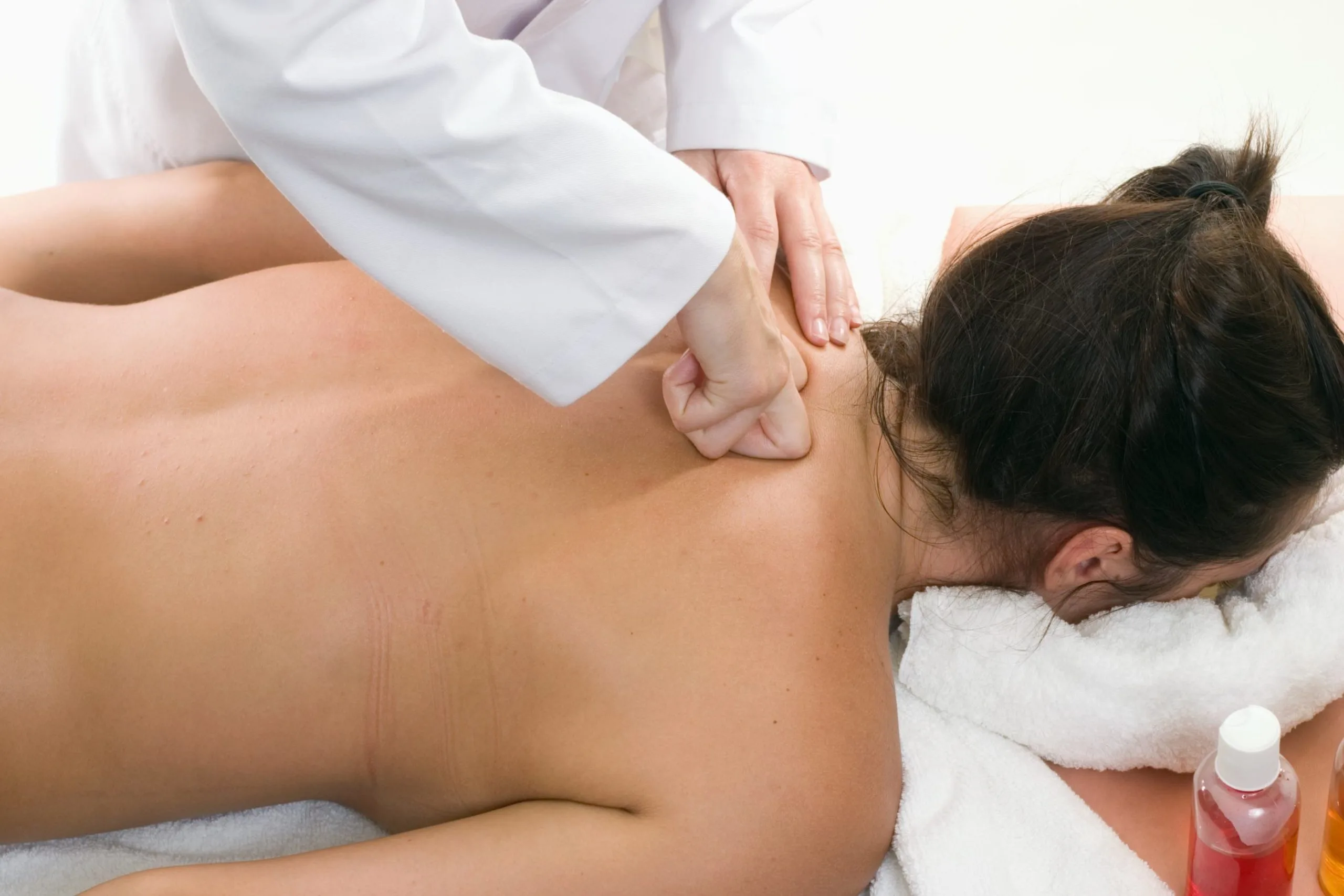 Massage therapist applying pressure to patient's shoulder and back during therapy session