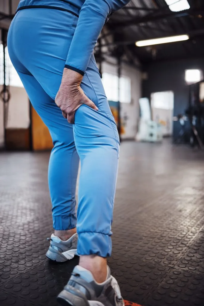 Person in blue workout clothes gripping thigh with hand while standing in gym