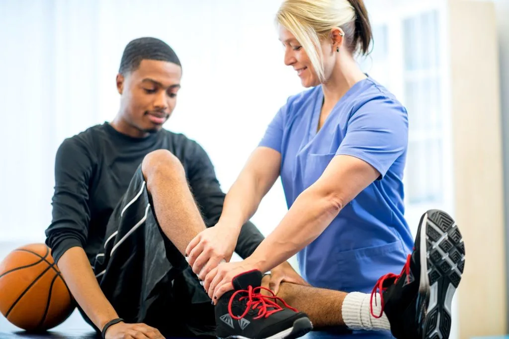 Physical therapist palpating male patient's leg and ankle with basketball nearby
