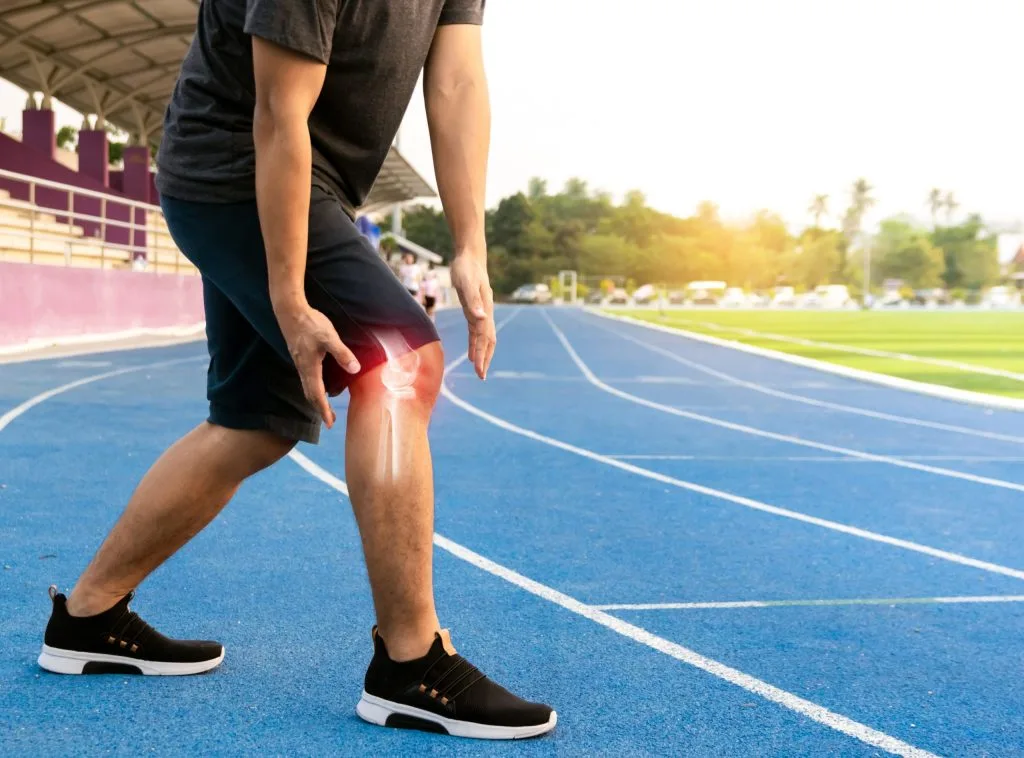 Runner on a track holding their knee with red highlight indicating pain or inflammation