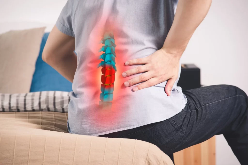 Person holding lower back with overlay showing deteriorated spine discs in red and blue