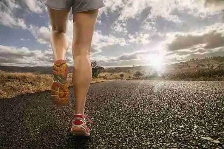 Runner's legs in motion on a sunny open road with fields in the distance