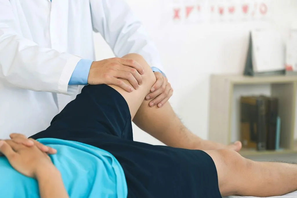 Chiropractor palpating patient's knee during examination in clinical setting