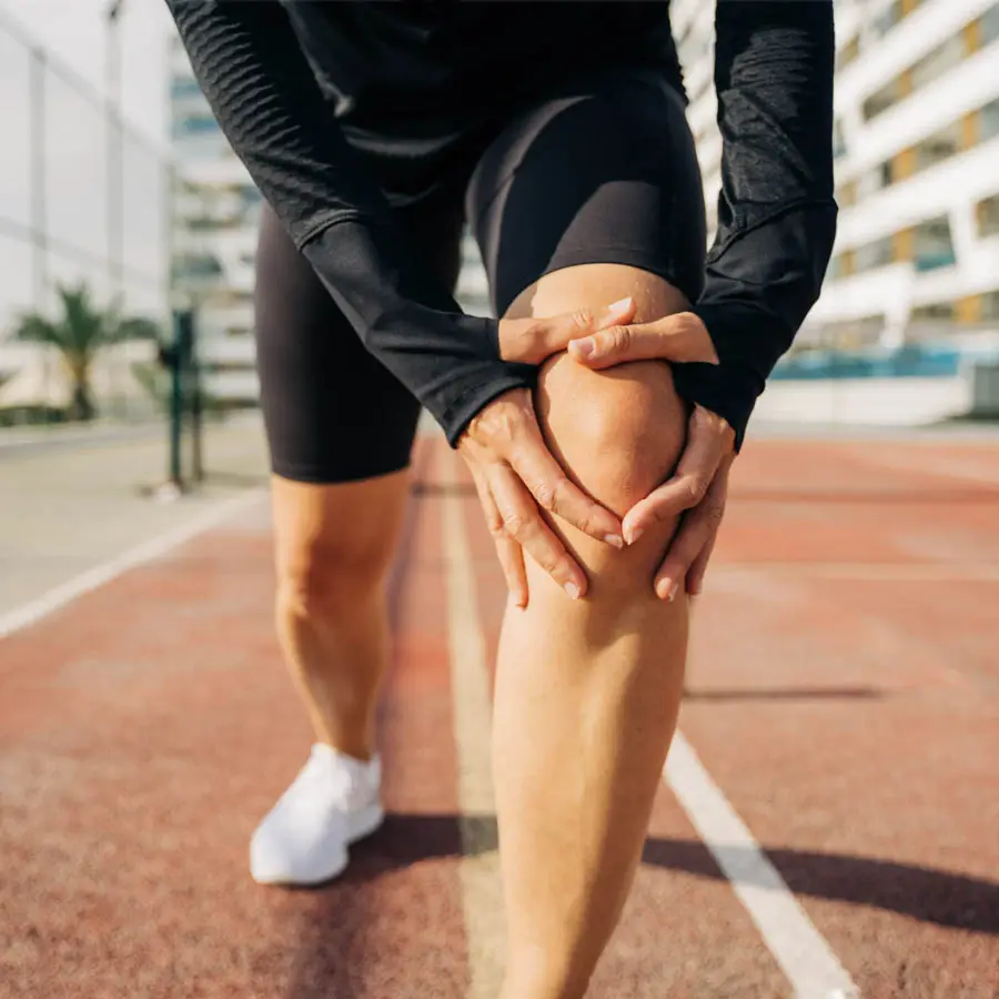 Runner holding knee outdoors after injury during physical activity