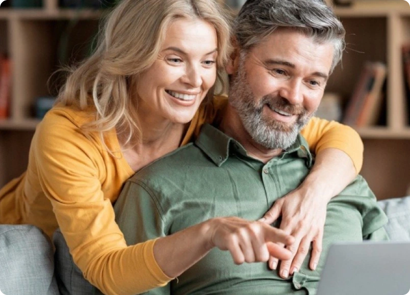 Couple smiling while reviewing financing options on laptop together