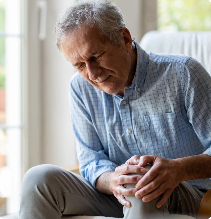 Older man sitting indoors, holding his knee in pain