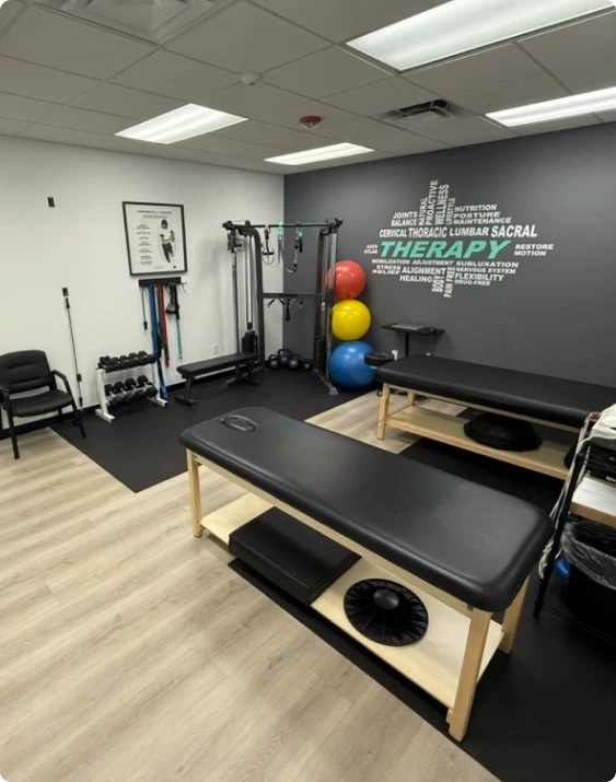 Physical therapy clinic interior with treatment table, exercise equipment, therapy balls, and anatomical wall decal