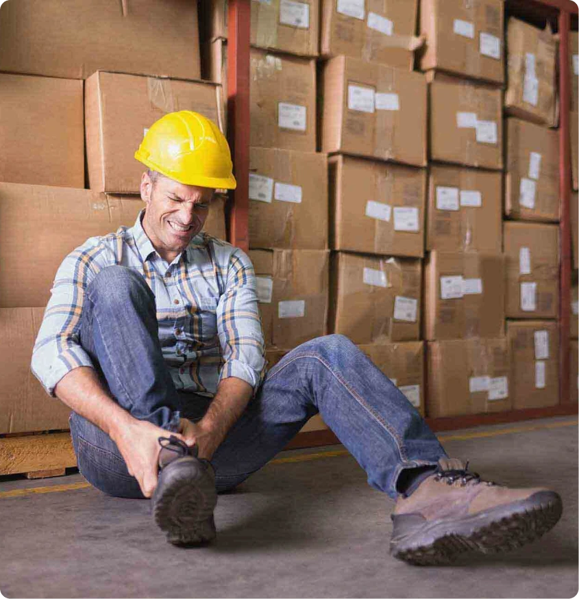 Warehouse worker in yellow hard hat holding his ankle after a workplace injury