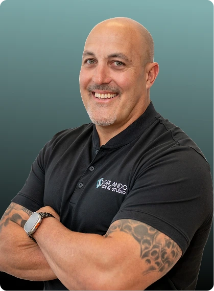 Man wearing Orlando Spine Studio branded black polo shirt with arms crossed, smiling at camera