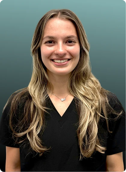 Woman with long blonde hair wearing black v-neck shirt, smiling at camera against teal background