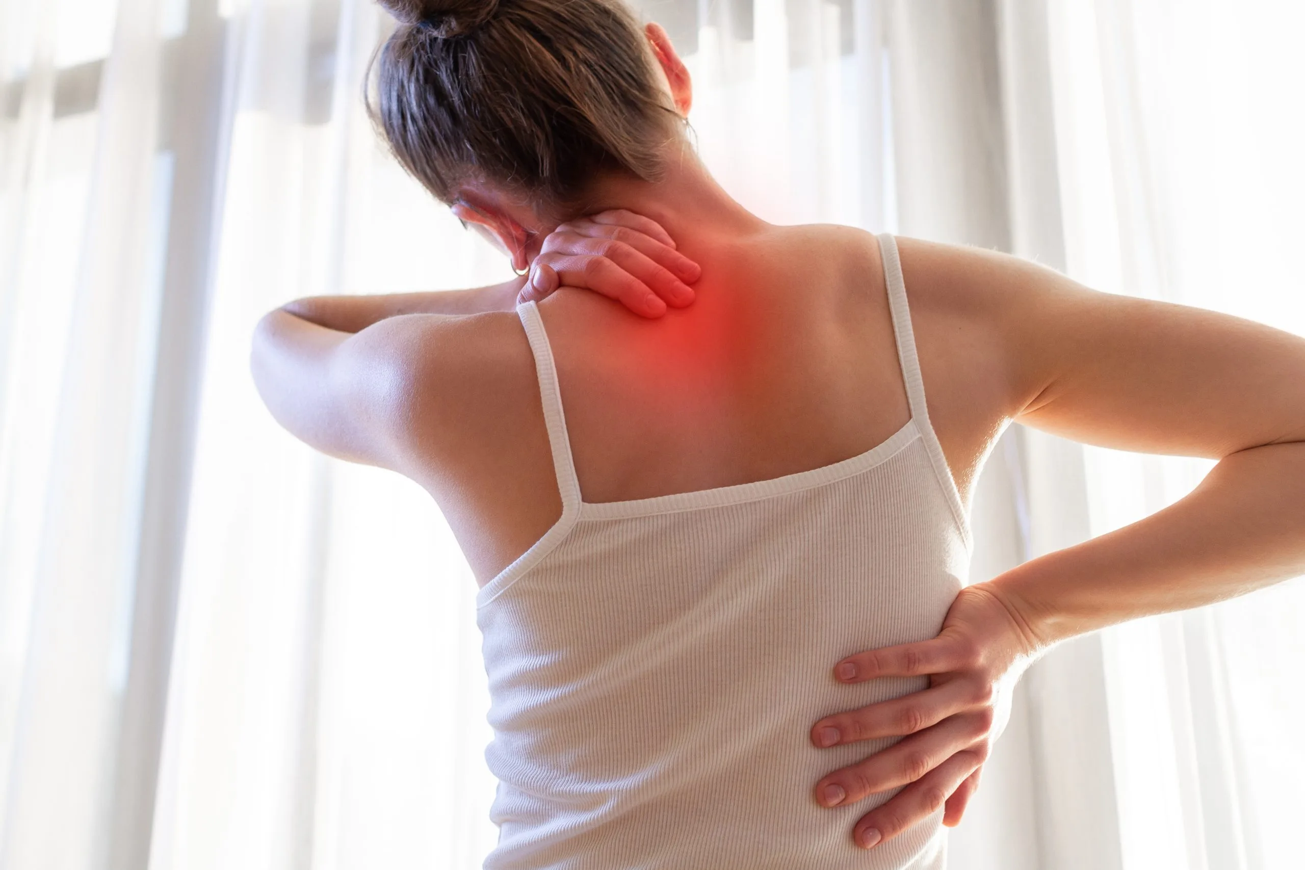 Woman from behind with red highlighted area on upper back and neck, holding lower back