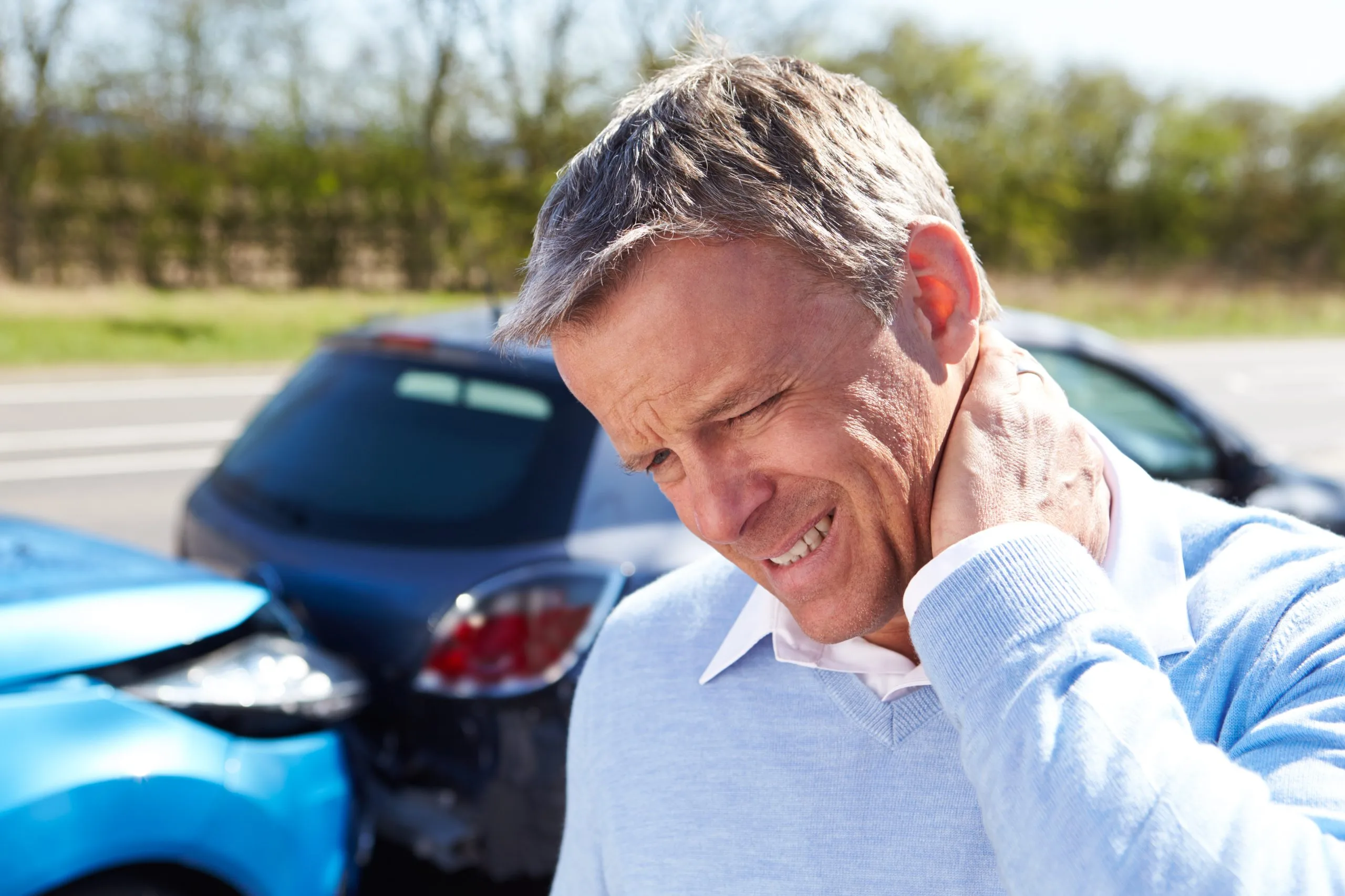 Man holding neck in pain at car accident scene with vehicles in background
