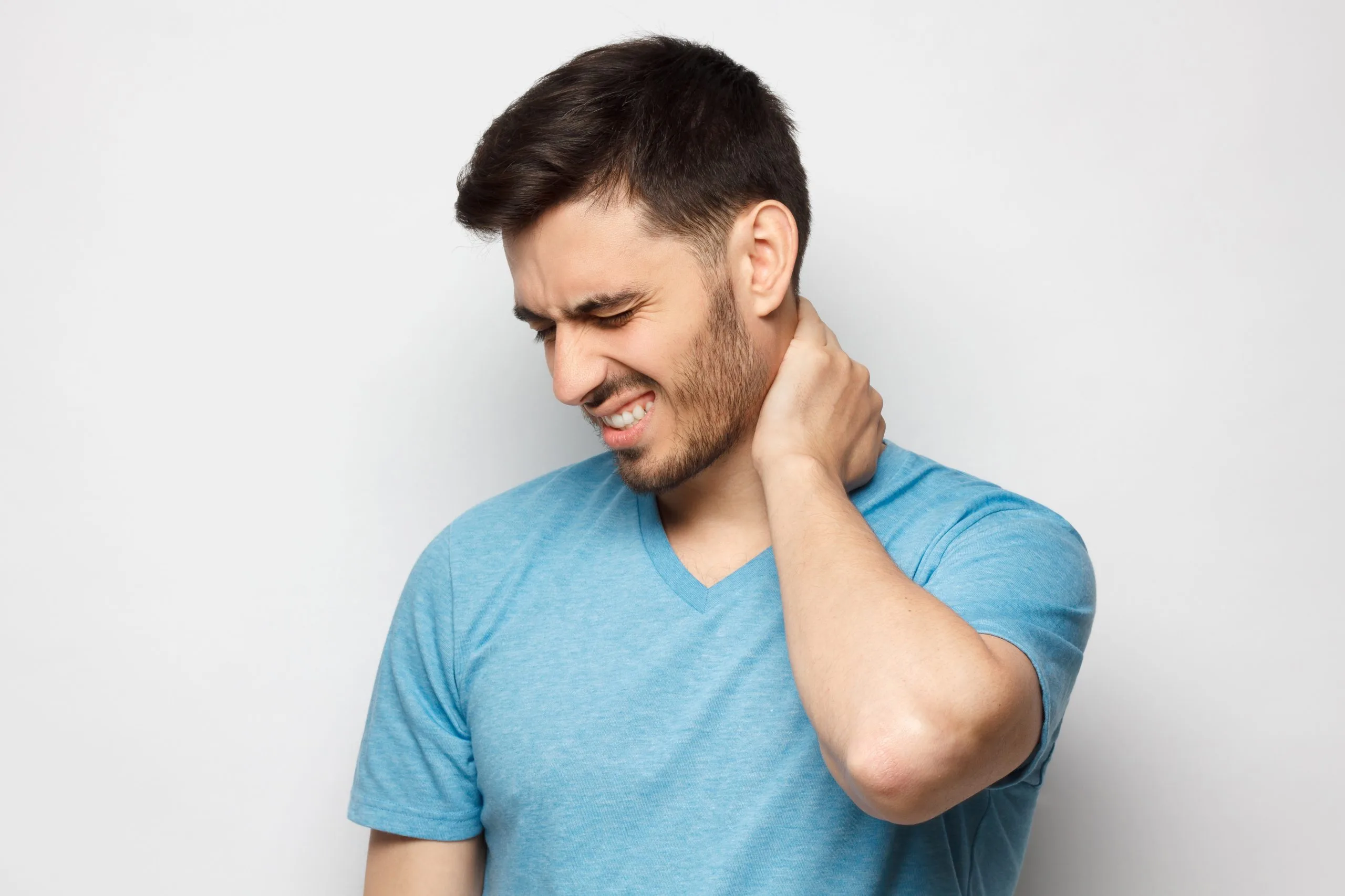 Man in blue shirt touching his neck with grimaced expression, indicating neck pain