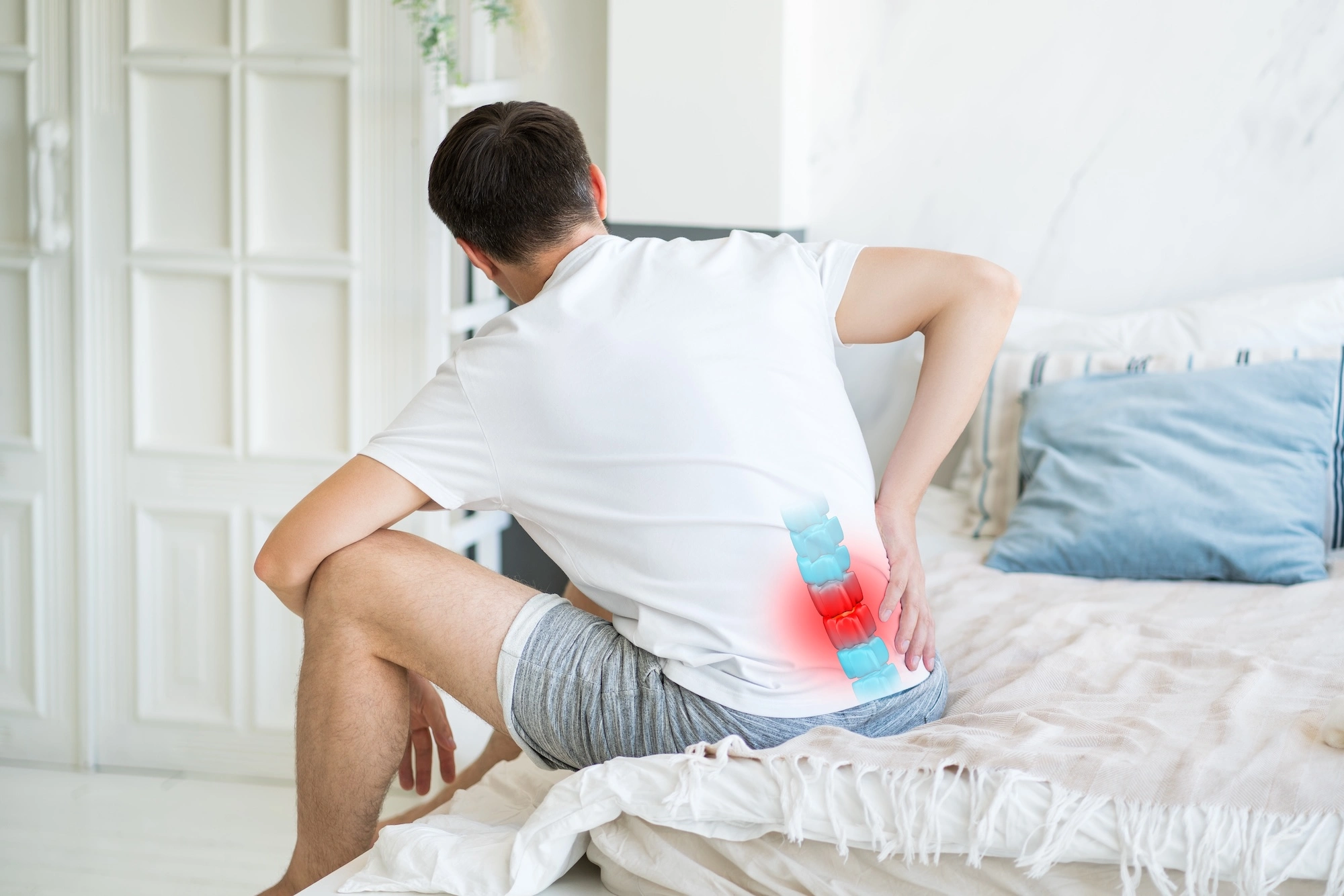 Man sitting on bed holding lower back with red highlight showing pain area