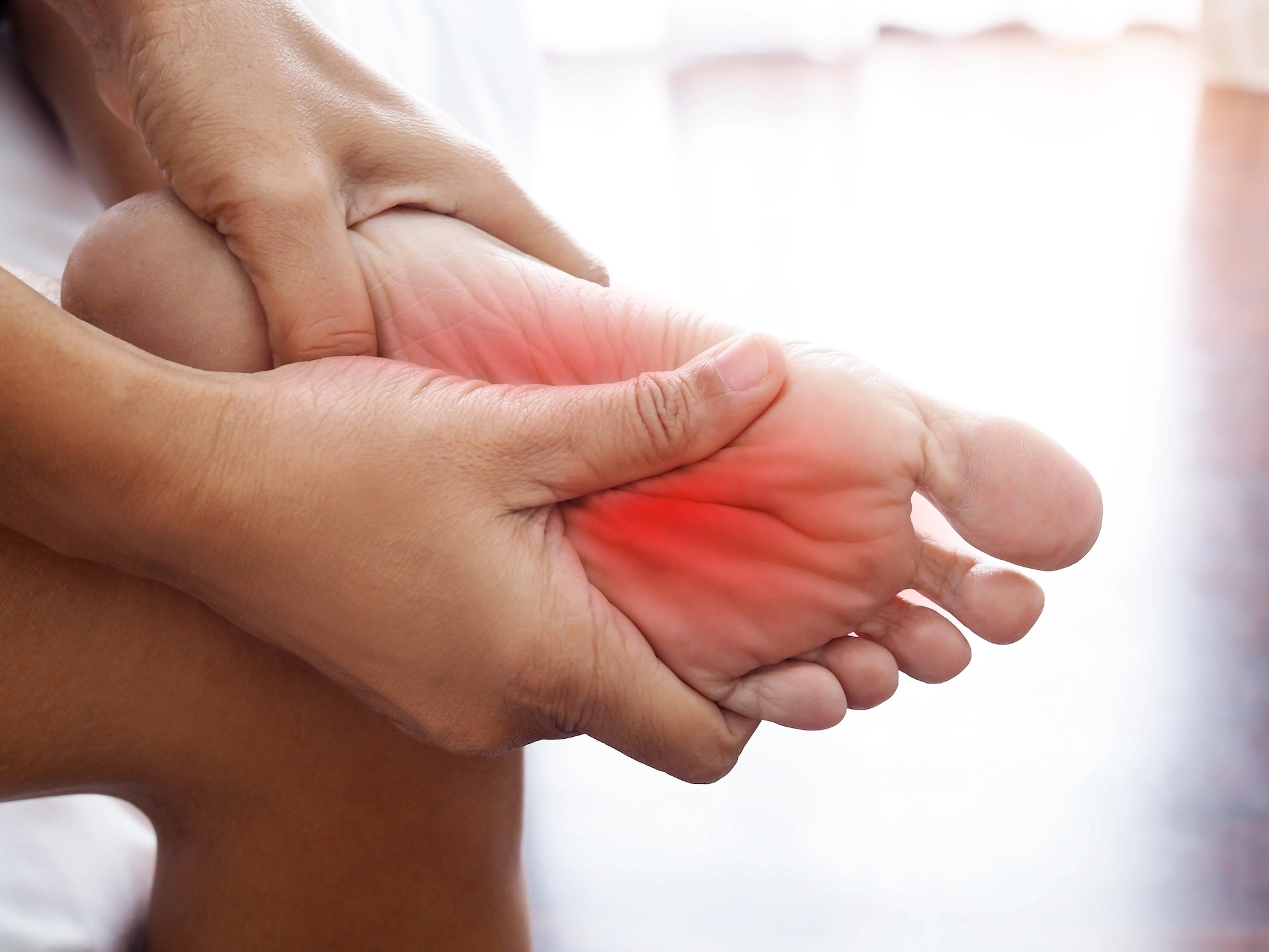 Hands holding foot with red highlight indicating pain or inflammation in arch area