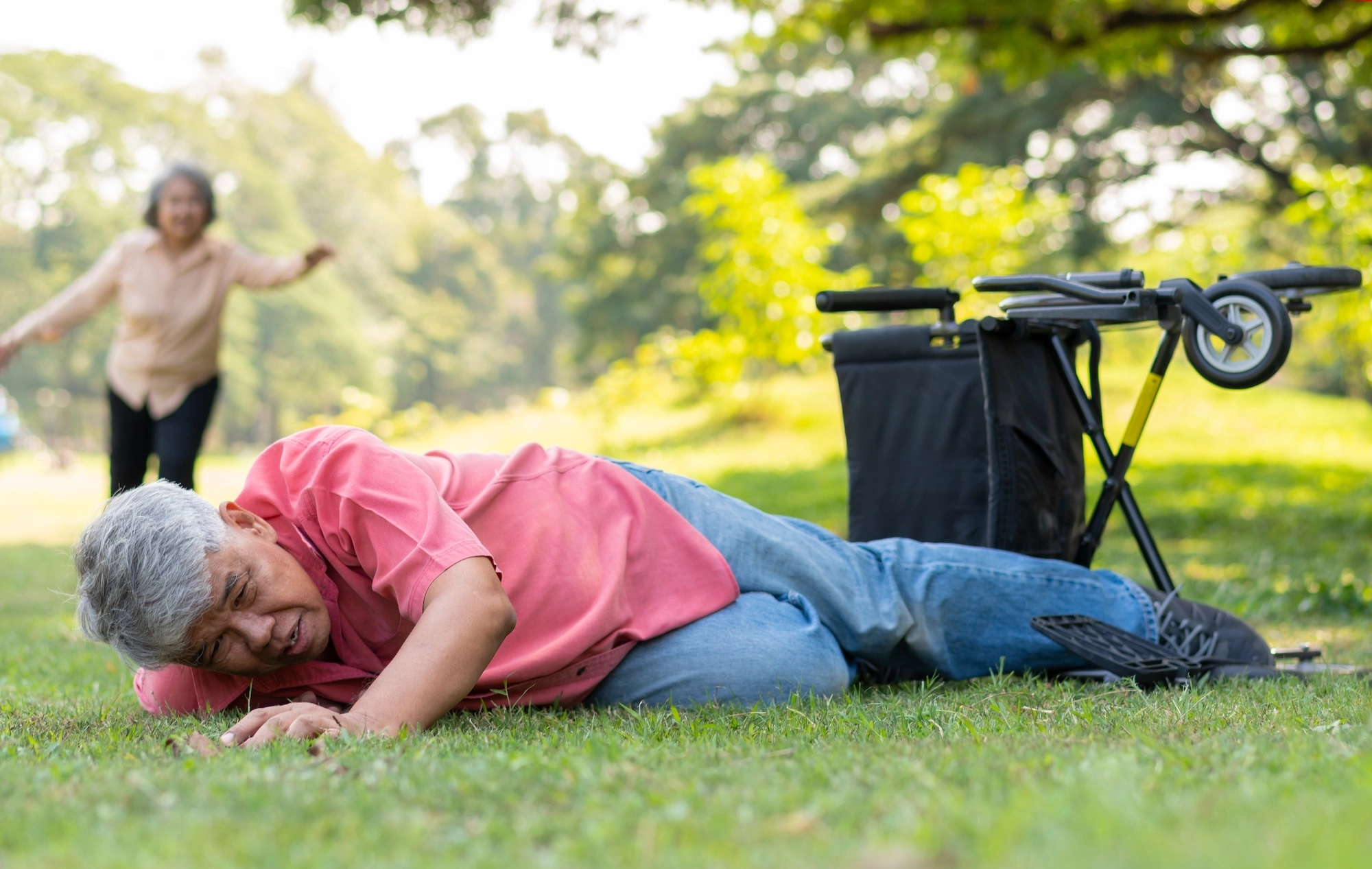 Older adult on ground near bicycle with person jogging in background, suggesting fall or injury