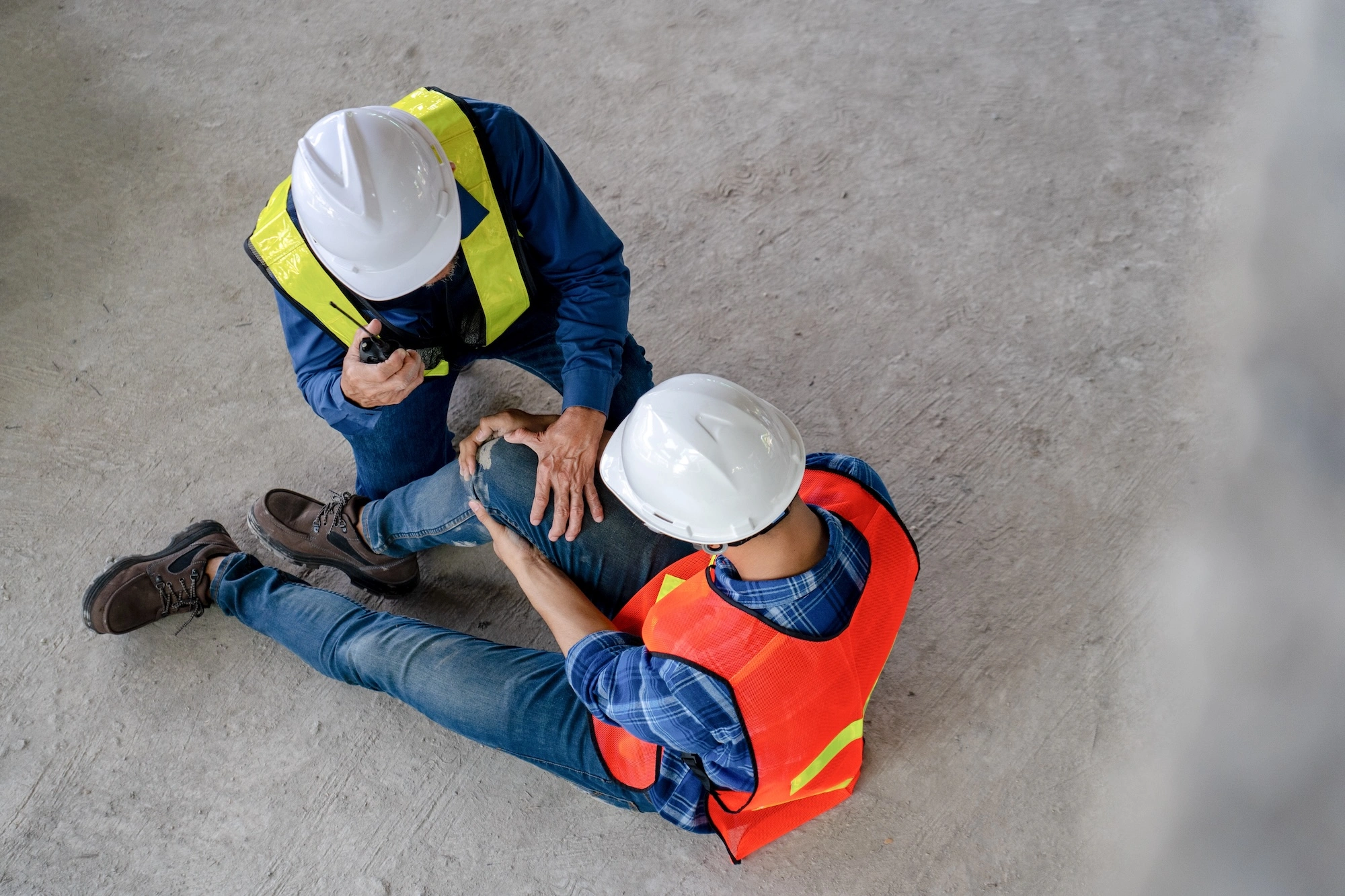 Worker assisting injured colleague on concrete floor at construction site