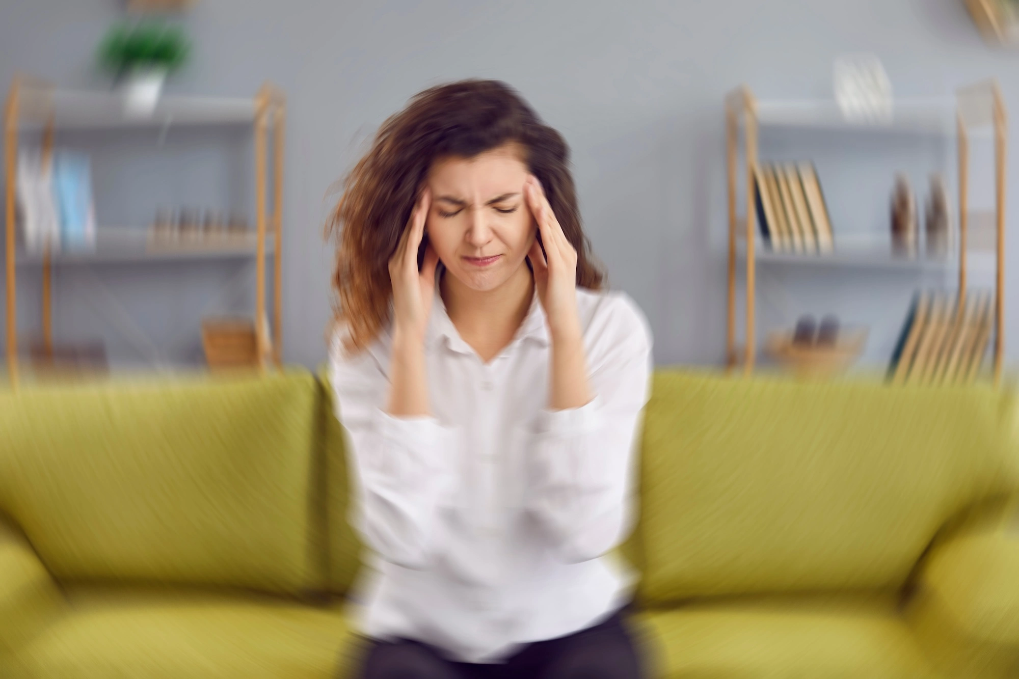 Woman on yellow couch holding head with both hands showing headache or stress