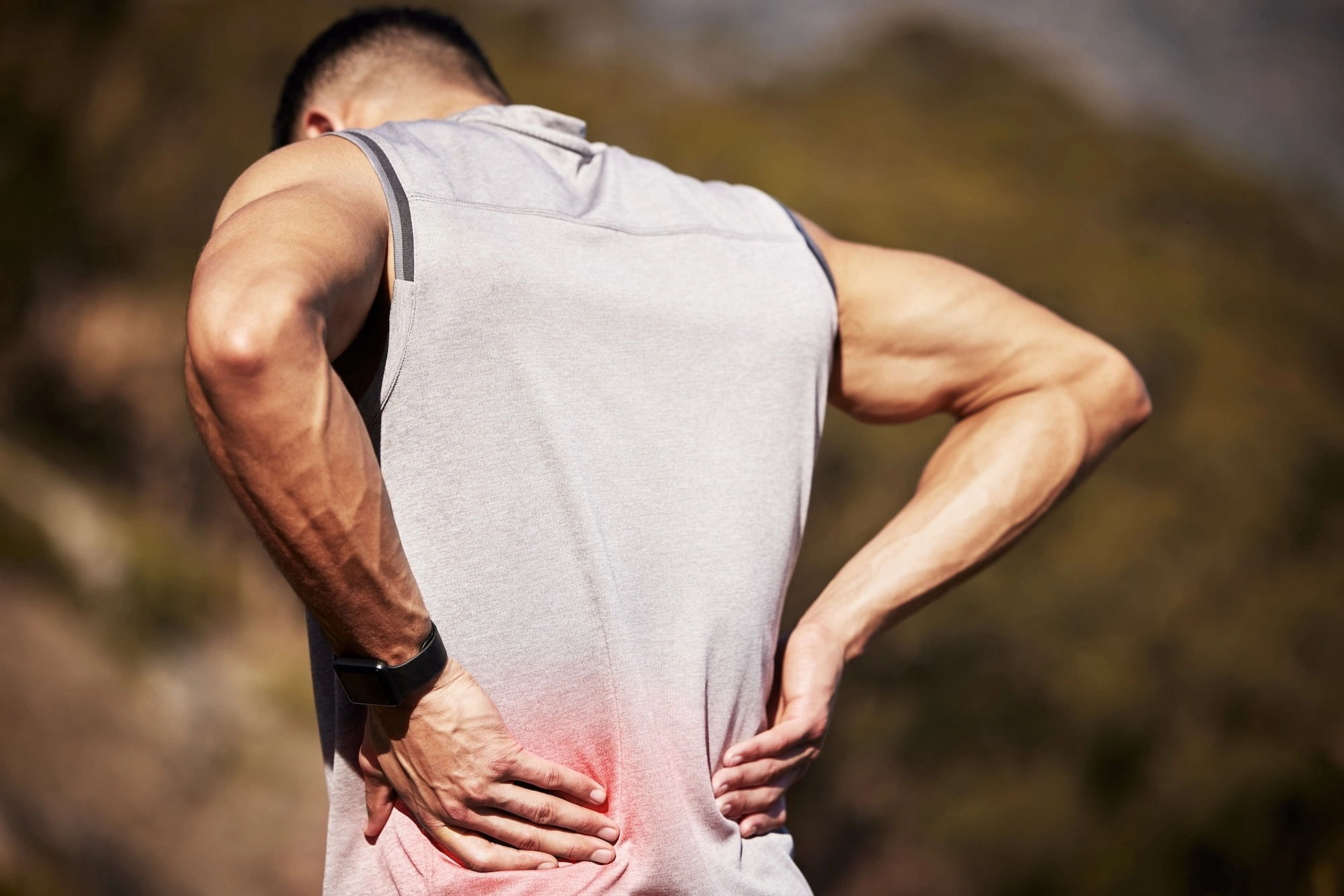 Person from behind with hands on lower back and upper back, red highlights showing pain areas