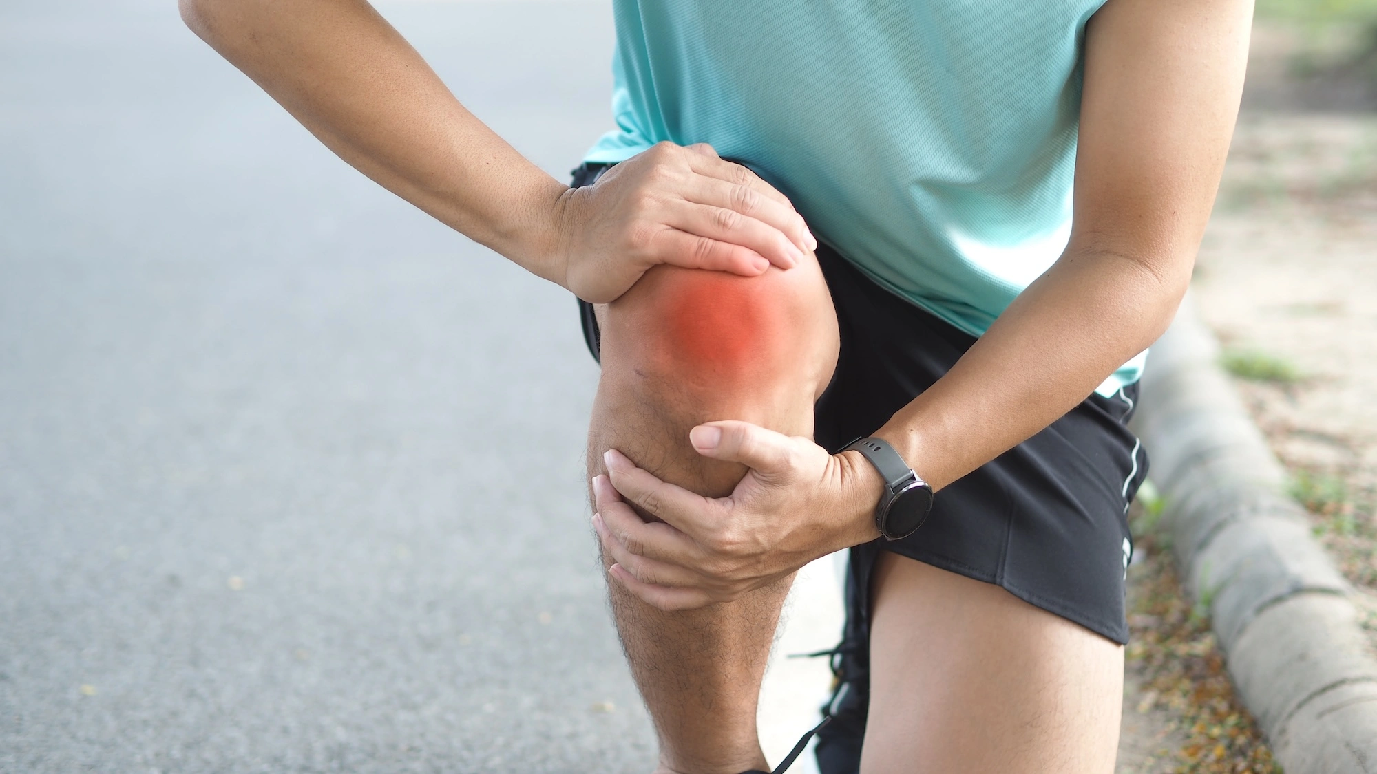 Person outdoors holding knee with red highlight indicating pain or inflammation