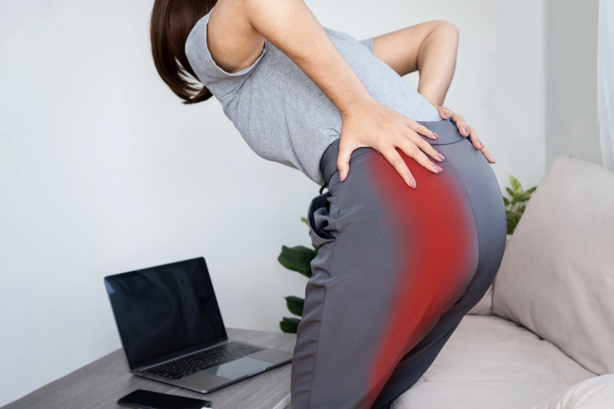 Woman sitting at desk holding lower back with red pain overlay showing lower back discomfort