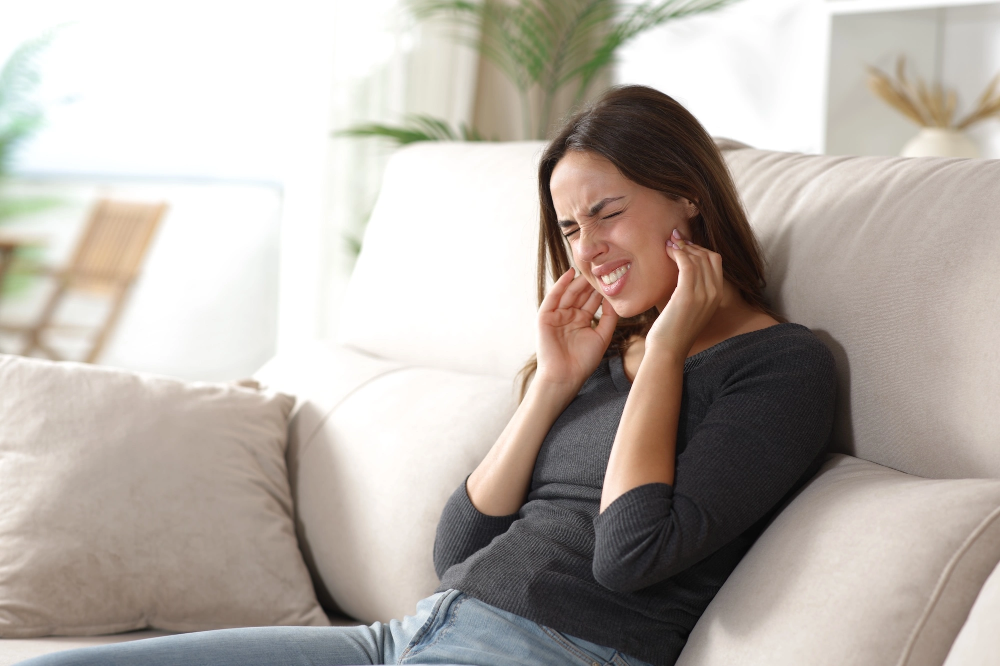 Woman on couch holding jaw with facial expression of pain or discomfort