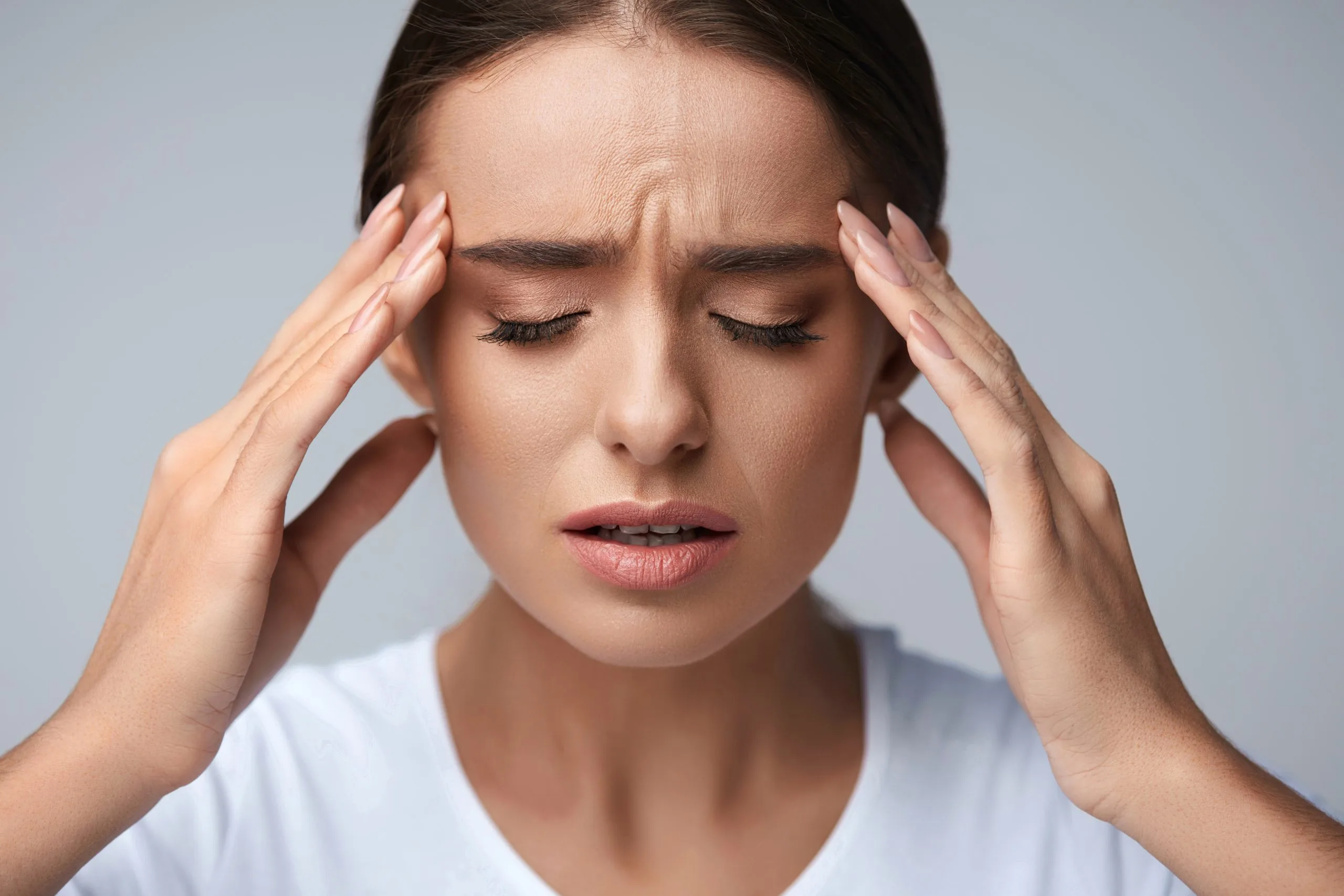 Woman holding her head with both hands, eyes closed, expressing headache pain
