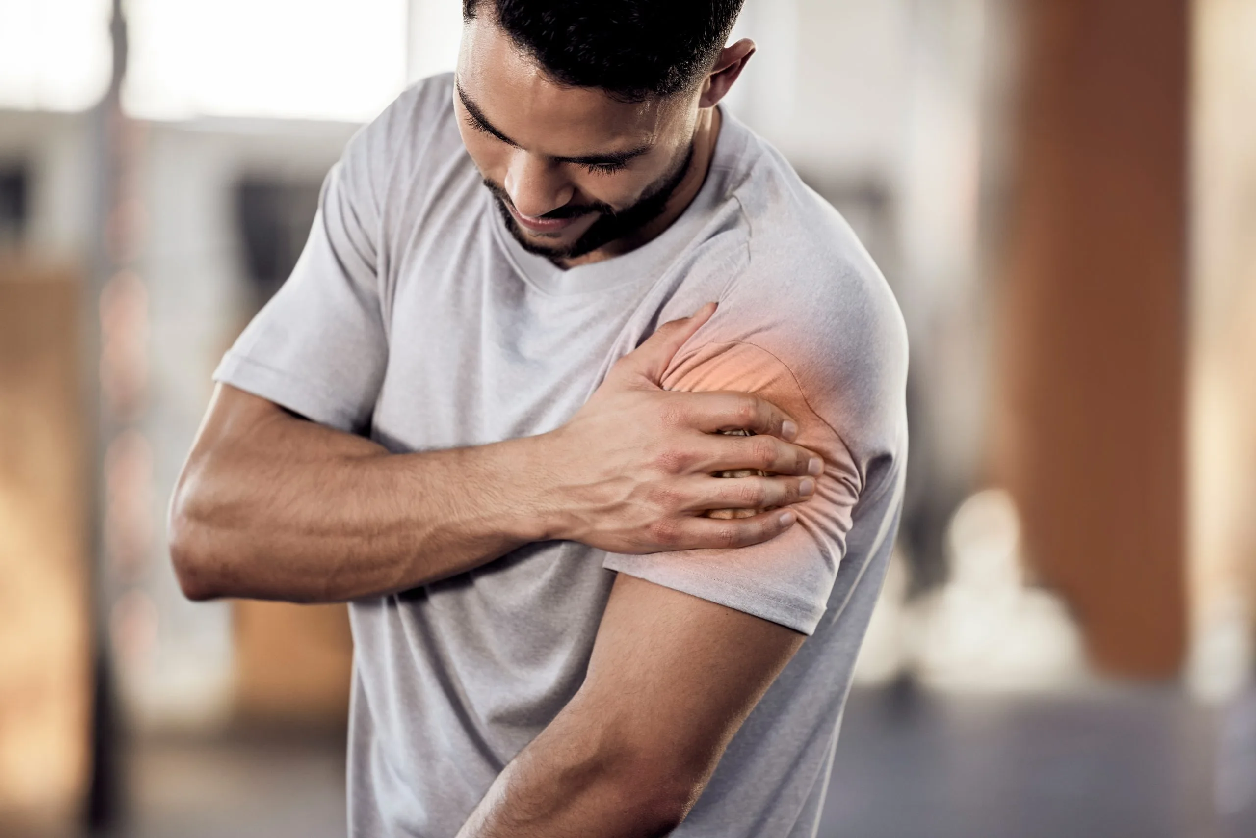 Man in light gray shirt holding his shoulder with orange highlighted pain area