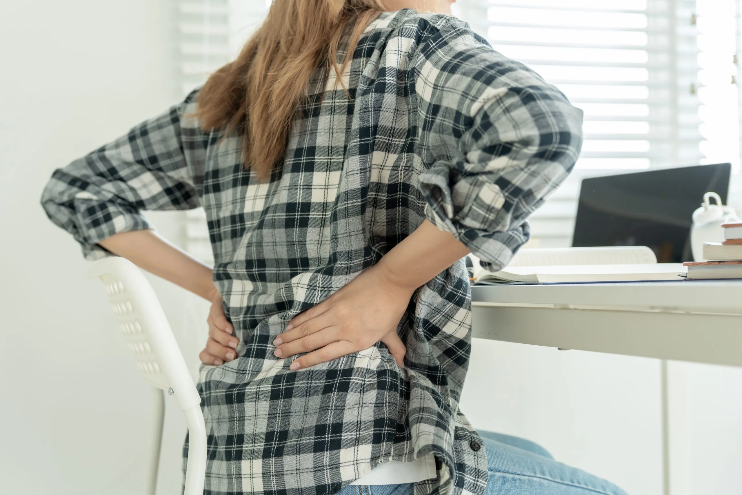 Woman at her desk holding her lower back from herniated disc pain